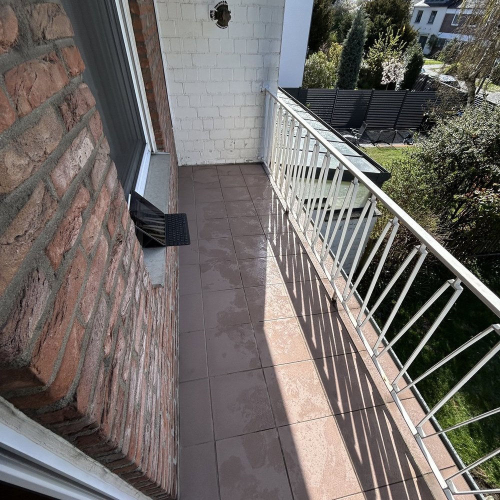 Schmaler Balkon mit Fliesenboden, Metallgeländer und Bohrloch in weißer Wand