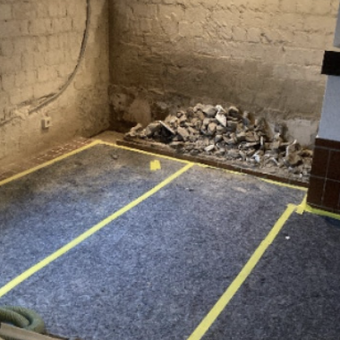 Kellerraum mit grauem Vlies auf dem Boden, Bauschutt an der Wand, Materialsäcke