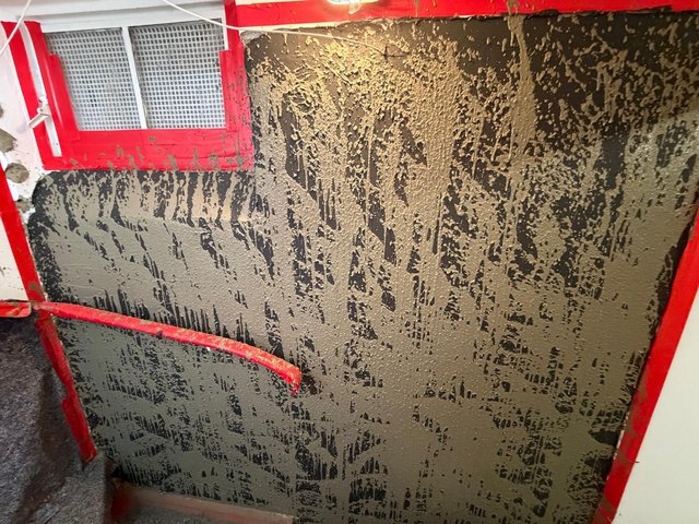 Schwarze Masse auf Kellerwand unter Fenster, Nahaufnahme
