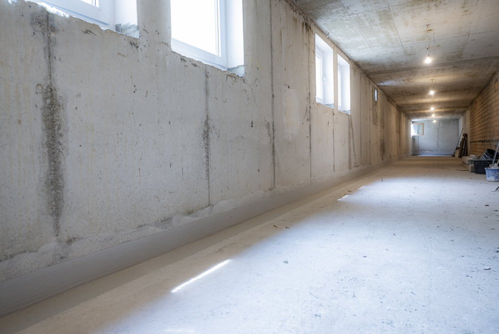 Langer Kellerraum mit Betonwänden, Fenstern und grauer Masse am Wandanschluss