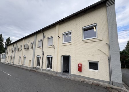 Lange helle Backsteinfassade mit Fenstern, Fallrohren und Eingang an Straße