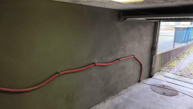 Rotes Kabel verläuft mit Halterungen an grauer Decke in Durchgang