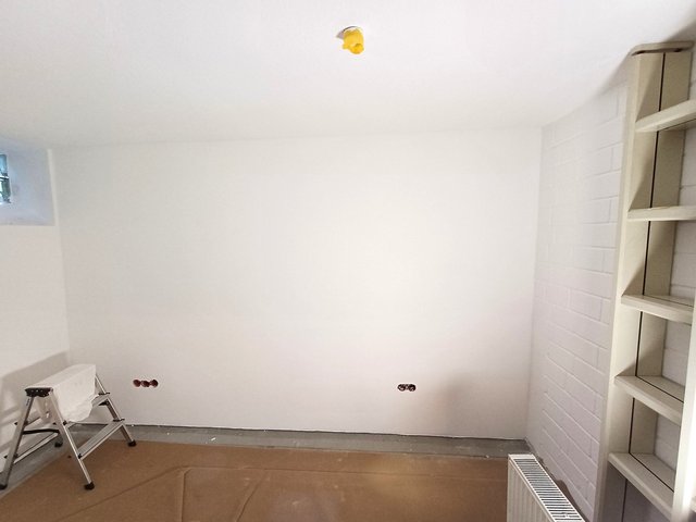 Leerer Raum mit weißer Wand, offenen Steckdosen und Abdeckpapier auf dem Boden.