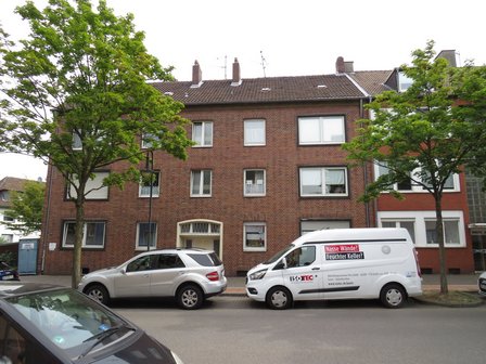 Mehrfamilienhaus aus Backstein an Straße, ISOTEC Transporter und Autos davor
