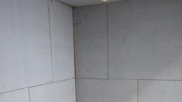 Leerer Raum mit hellen Platten an Wänden und Decke, Boden mit gelben Klebestreifen