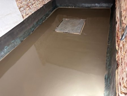 Frische graue Masse auf Bodenfläche mit quadratischer Öffnungsabdeckung im Kellerraum