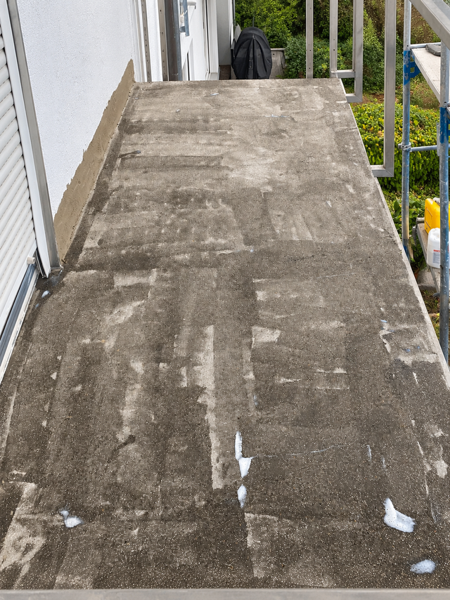 Balkonboden mit grauen Platten und hellen Kleberesten, seitlich Geländer