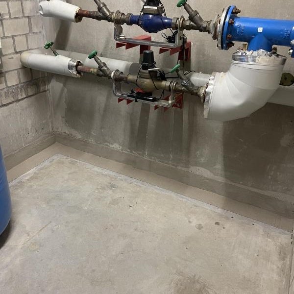 Rohrleitungen mit Armaturen und Ventilen an Betonwand in Technikraum