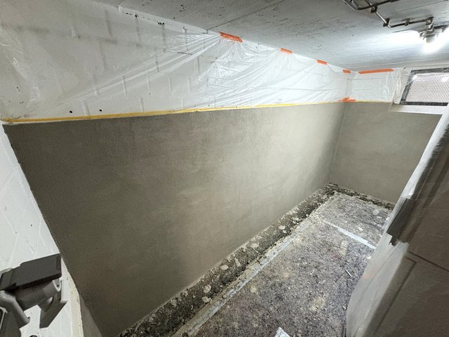 Abgeklebte Folie schützt Decke, graue Masse auf Kellerwand aufgetragen.