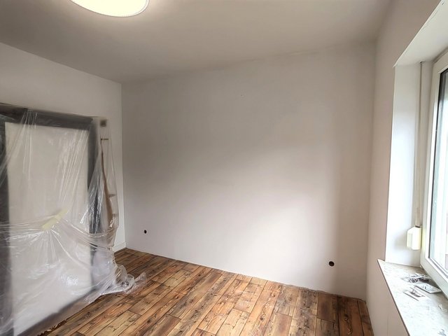 Leerer Raum mit weißer Wand, Holzoptikboden und abgedecktem Möbelstück