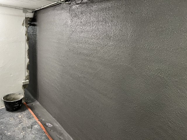 Schwarze Masse auf Kellerwand aufgetragen, Eimer am Boden