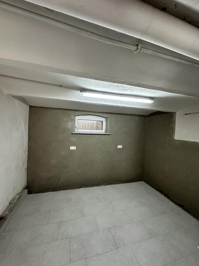 Kellerraum mit grauen Wänden, kleinem Fenster und Deckenleuchte, Fliesenboden