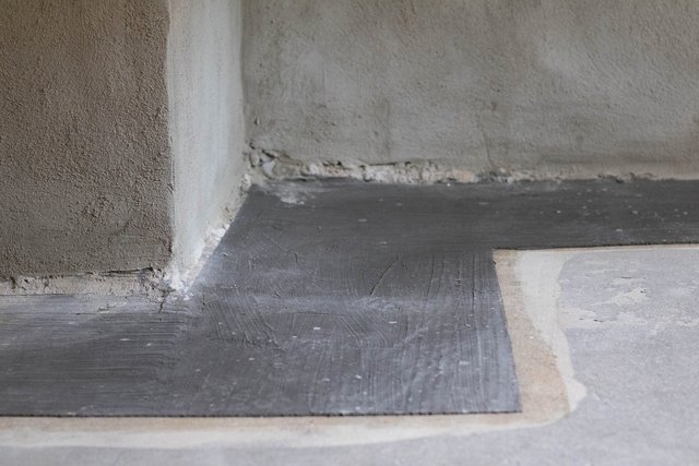 Schwarze Masse auf Bodenanschluss an verputzter Wand, Nahaufnahme