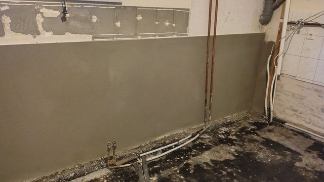 Frisch aufgetragene graue Masse an Kellerwand, sichtbare Rohre und Leitungen am Boden