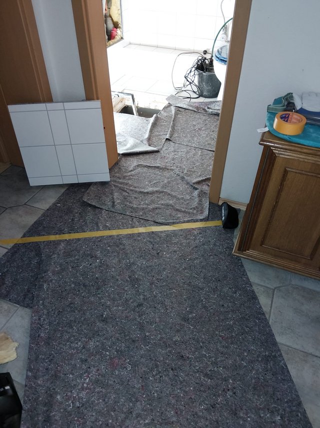 Boden im Flur mit Schutzvlies abgedeckt, geoeffnete Bodenfliesen im Raum dahinter