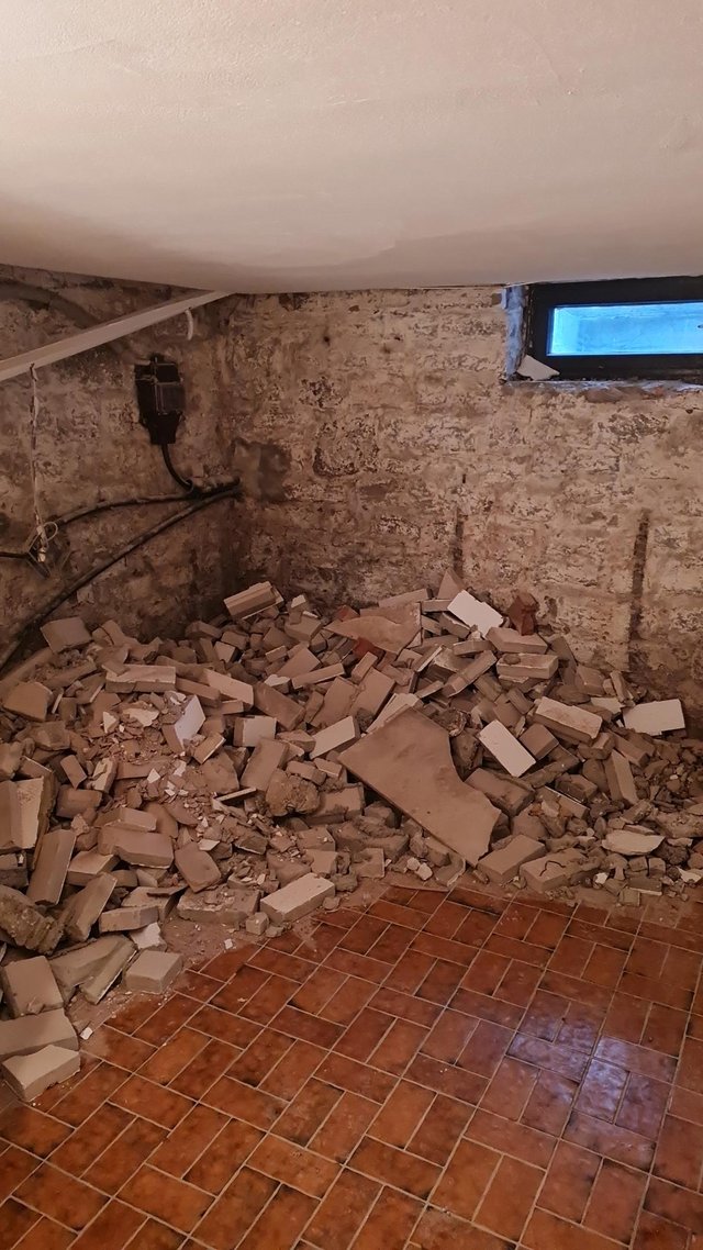 Abbruchschutt aus Mauersteinen und Putzresten in Kellerraum vor freigelegter Wand