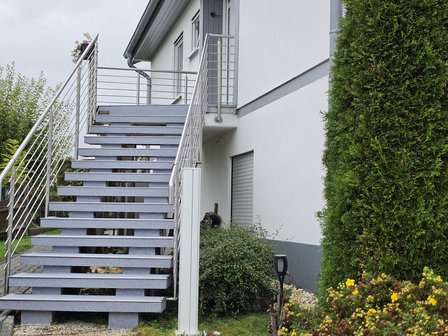 Außentreppe mit grau gesprenkelten Stufen und Edelstahlgeländer vor weißer Hausfassade