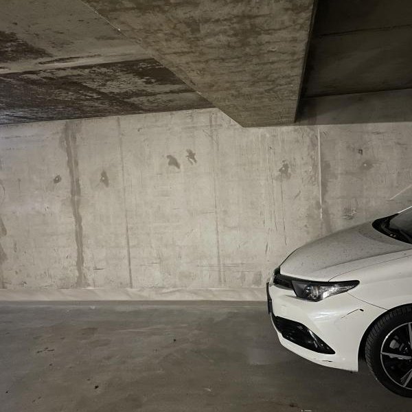 Leere Tiefgarage mit Betonwand und teilweisem weißen Auto im Vordergrund.