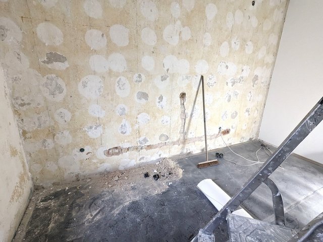 Freigelegte Wand mit weißen Spachtelflecken, Boden mit Bauschutt und Besen