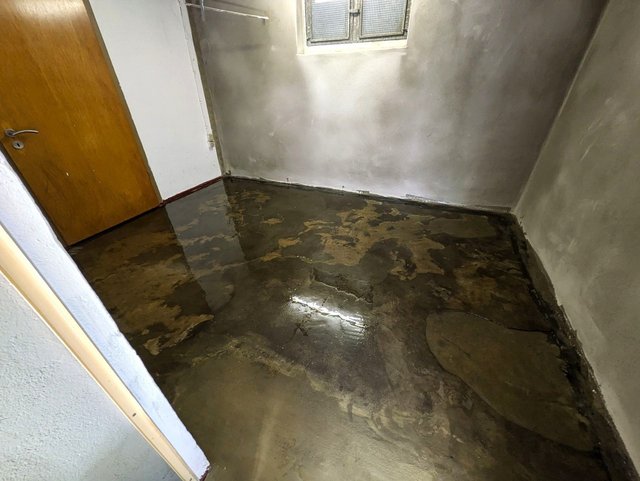 Nasser Betonboden mit Pfützen in kleinem Kellerraum, Tür und Fenster sichtbar