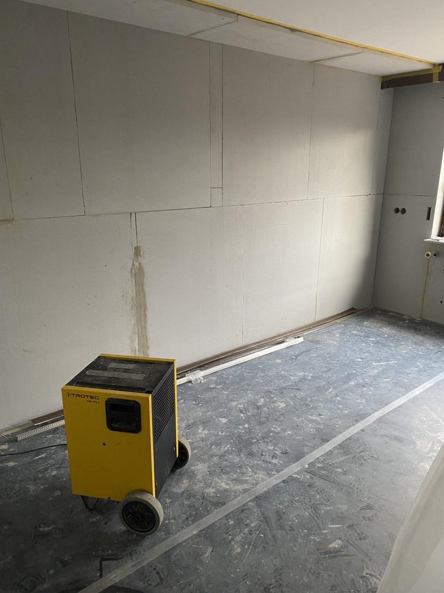 Gelber Bautrockner vor heller Plattenwand in leerem Raum