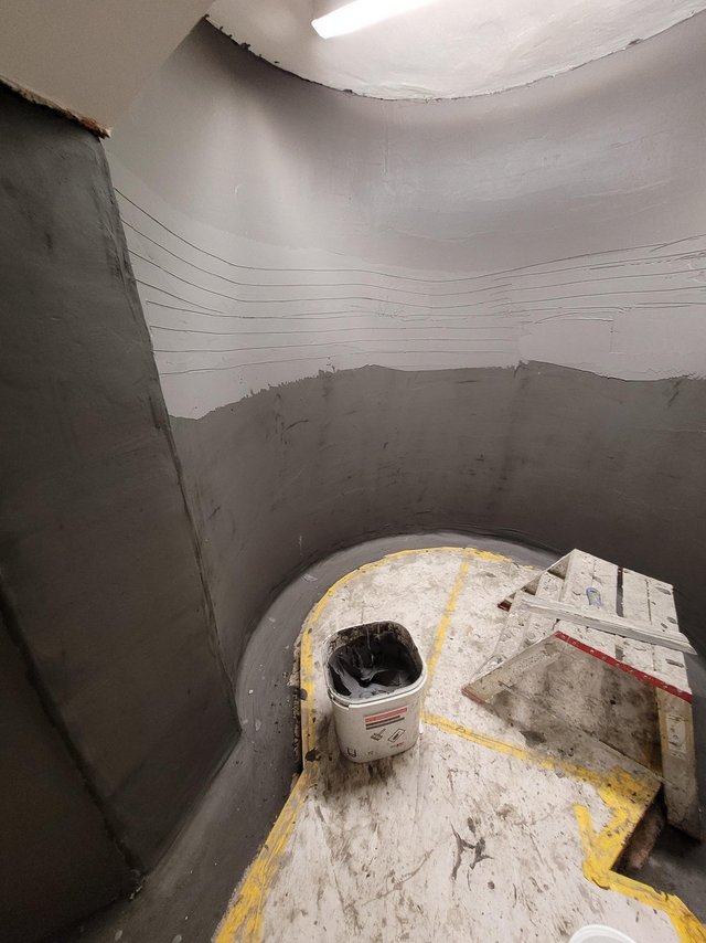 Dunkelgraue Beschichtung an runder Betonwand, Eimer und Leiter im Raum