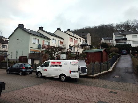 ISOTEC Transporter parkt vor Reihenhäusern in Wohnstraße, Hanglage mit Bäumen im Hintergrund.