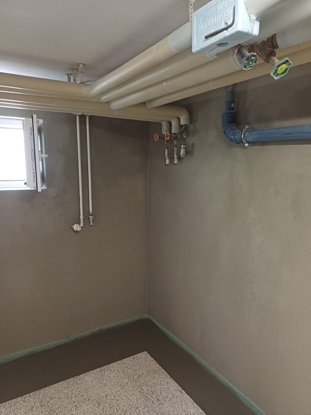 Kellerraum mit grauen Wänden, Fenster und freiliegenden Rohrleitungen unter der Decke