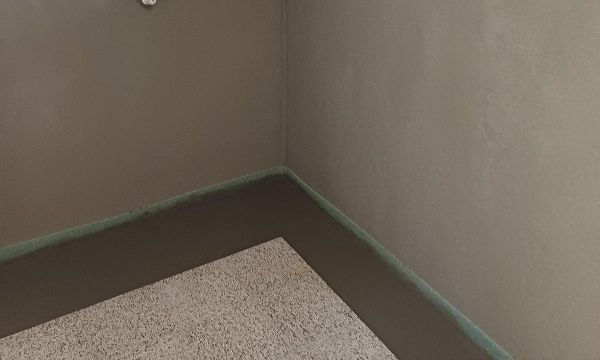 Kellerraum mit grauen Wänden, Fenster und freiliegenden Rohrleitungen unter der Decke