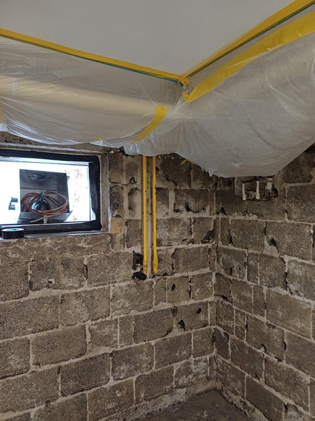 Abgeklebte Folie unter Decke, unverputzte Kellerwand aus Betonsteinen mit Leitungen