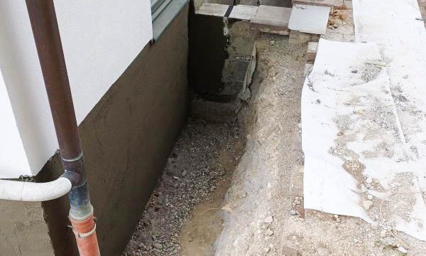 Freigelegter Gebäudesockel neben Eingang, Erdgraben mit Schotter und Schutzfolie.