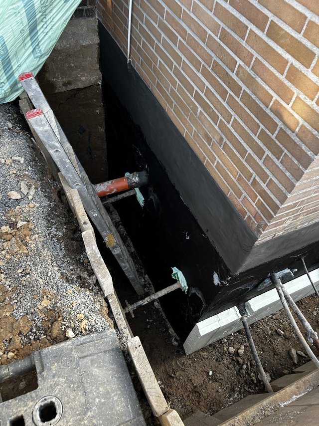 Freigelegte Hauswand mit schwarzer Masse im Erdreich abgedichtet