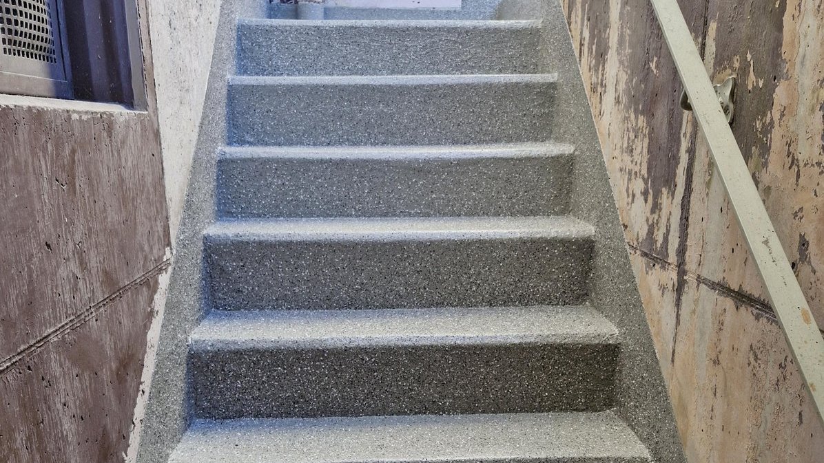 Grau beschichtete Betontreppe mit Metallhandlauf zwischen zwei Wänden