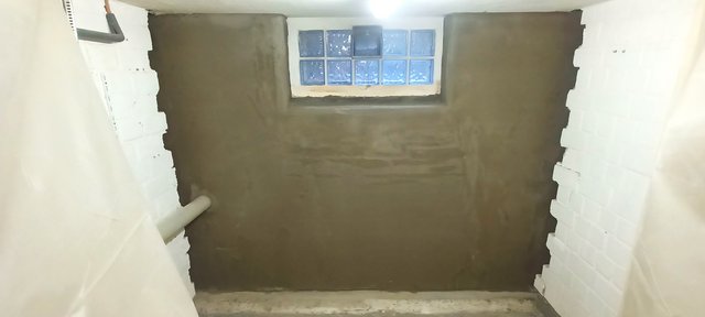 Mit brauner Masse beschichtete Kellerwand mit Glasbausteinfenster.