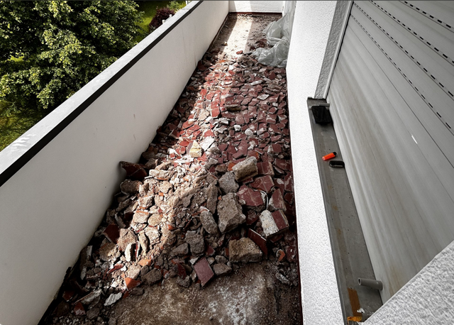 Bauschutt aus roten Fliesen und Beton auf schmalem Balkon