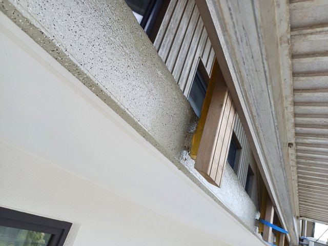 Gesprenkelte graue Masse auf Wand neben Holzlatten und dunklem Fenster, schräge Nahaufnahme