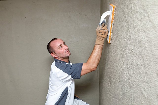 Arbeiter glättet graue Masse auf Wand