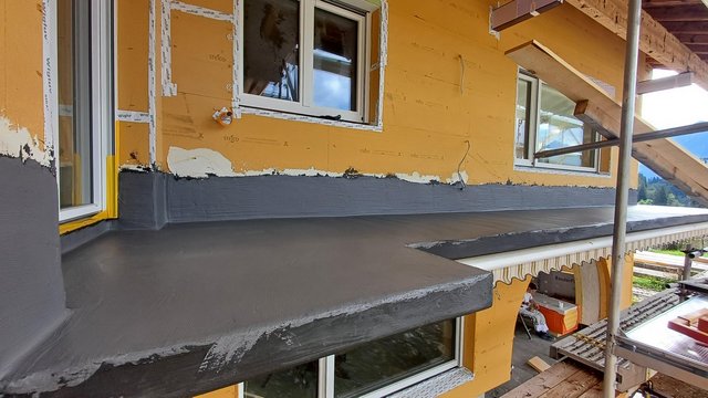 Graue Masse auf Balkon und Wandsockel aufgetragen, Arbeiter sitzt im Hintergrund