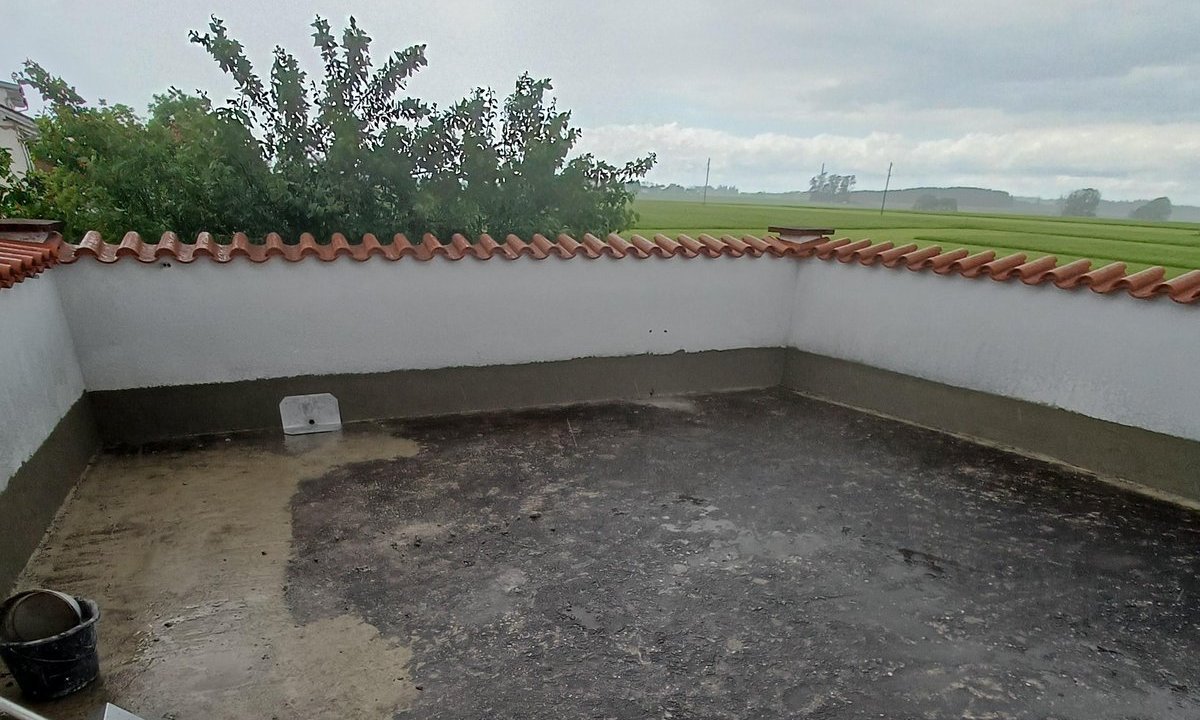 Flachdachterrasse mit schwarzer Masse auf Boden, niedrige Mauer mit Ziegelabdeckung.