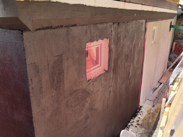 Schwarze Masse auf Gebäudeaußenwand mit kleinem Fenster aufgetragen