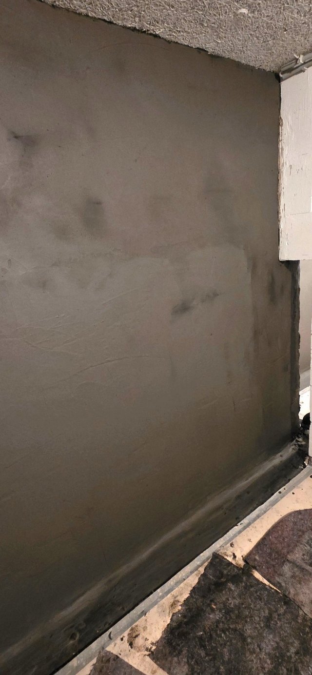 Graue Wandfläche mit dunklen Flecken und schwarzer Masse im Sockelbereich