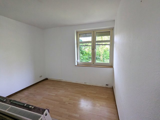 Leeres Zimmer mit weißer Wand, Fenster und hellem Laminatboden, Blick ins Grüne
