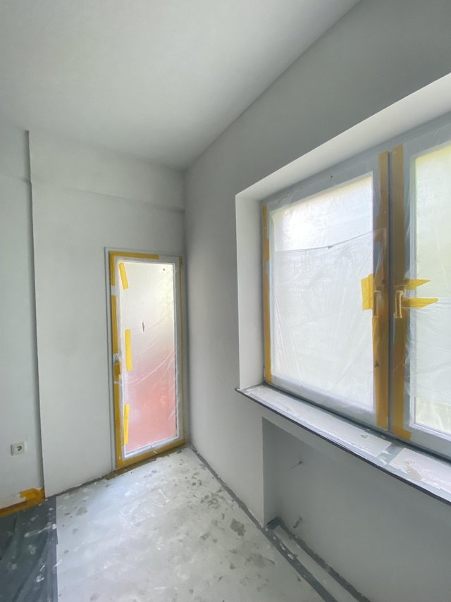 Abgeklebte Fenster und Balkontür in hellem Zimmer, frisch bearbeitete Wände