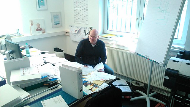 Carsten Pläsken im Büro am Schreibtisch vor den Bergen von Post und zu erstellenden Angeboten.