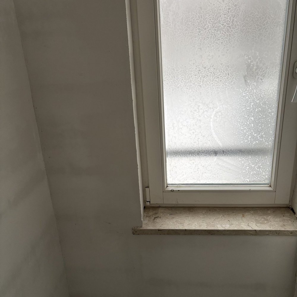 Fenster mit matt gemusterter Scheibe über heller Wandfläche.