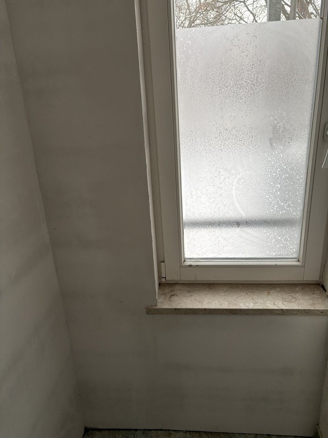 Fenster mit matt gemusterter Scheibe über heller Wandfläche.