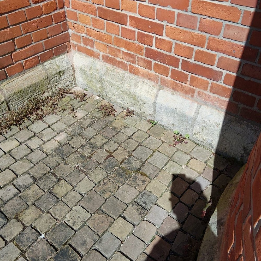 Ziegelmauerecke mit grauem Sockel und Pflastersteinen, Laub am Rand.