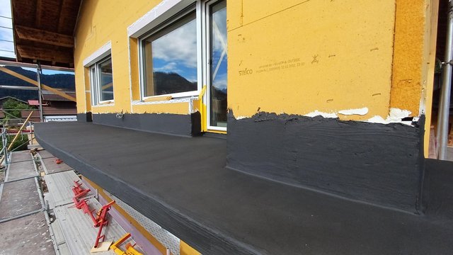 Schwarze Masse auf Fensterbank und Fassade aufgetragen, gelbe Dämmplatten an Hauswand.