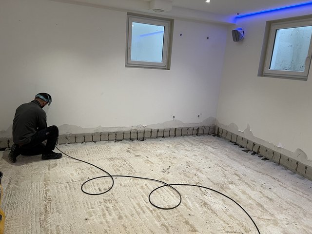 Arbeiter bearbeitet Sockelbereich im Kellerraum, Boden freigelegt