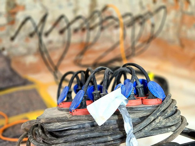 Mehrfachsteckdose mit blauen Steckern und aufgewickelten schwarzen Kabeln, Nahaufnahme